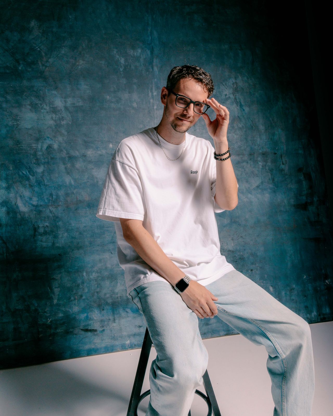 Editorial portrait man in white t-shirt and glasses on stool teal background — Thomas Habr photographer